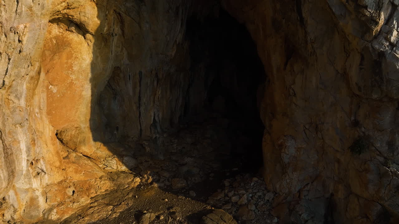 Aerial view rising in front of cave carved in a mountain wall, sunrise in Greece