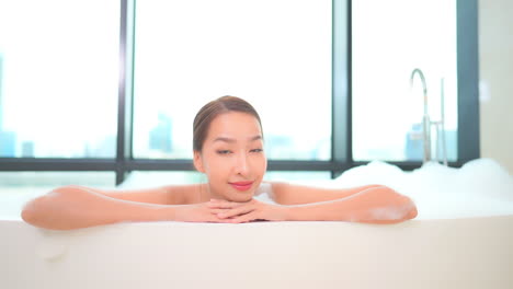 close-up of an attractive woman in a bubble bath with her arms and chin resting on the edge of the tub