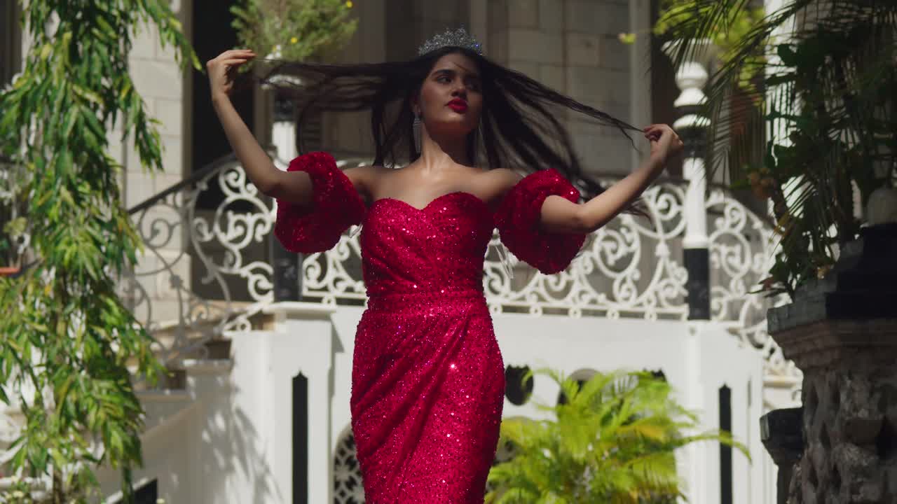 Entre los históricos muros de un castillo caribeño, una joven con un vestido carmesí encarna la gracia y la compostura.