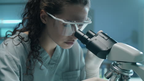 Female-Biologist-Examining-Plant-with-Microscope-in-Lab