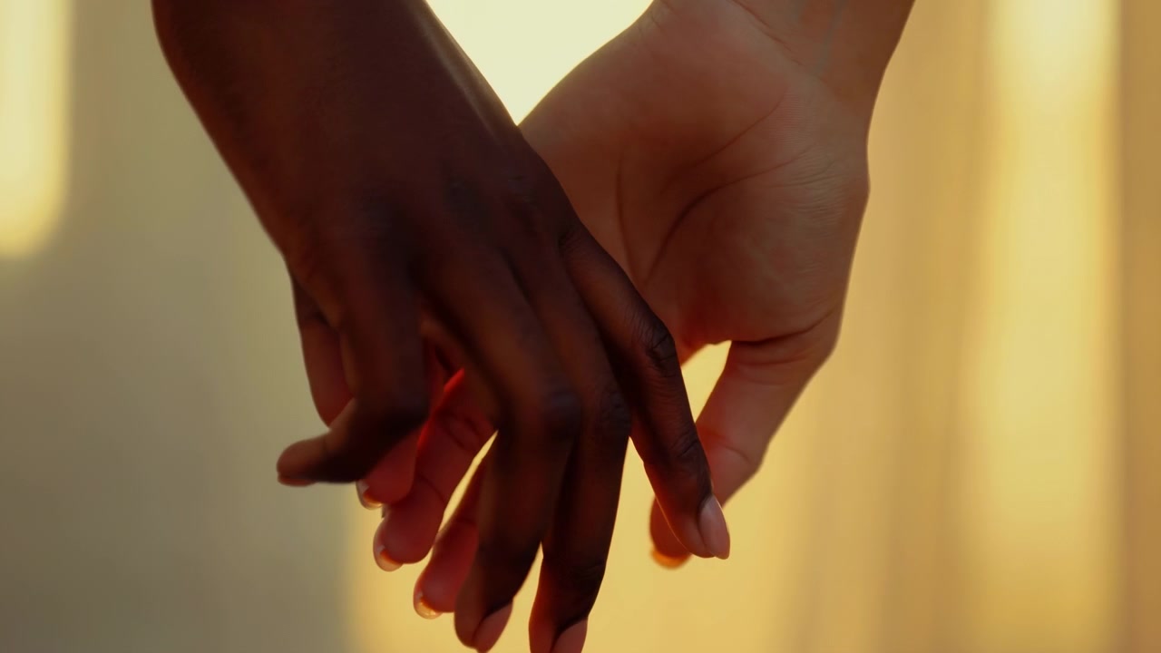 Close-up motion shot of two hands held together with interlaced fingers against warm backlit interior