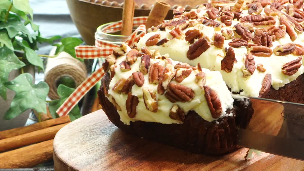 Baking a carrot cake loaf with cream cheese icing and topped with roasted salted pecans. Making a Autumn dessert with carrots, flour, sugar, nuts and frosting with a top down view that's close up.