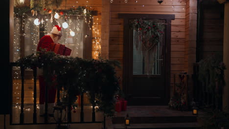 plan general santa claus lleva y entrega un regalo en sus manos en invierno y entra en la casa con guirnaldas y decoraciones de navidad. en diciembre en la víspera de navidad