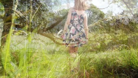 Composite-video-of-grass-moving-against-rear-view-of-caucasian-woman-walking-in-the-forest