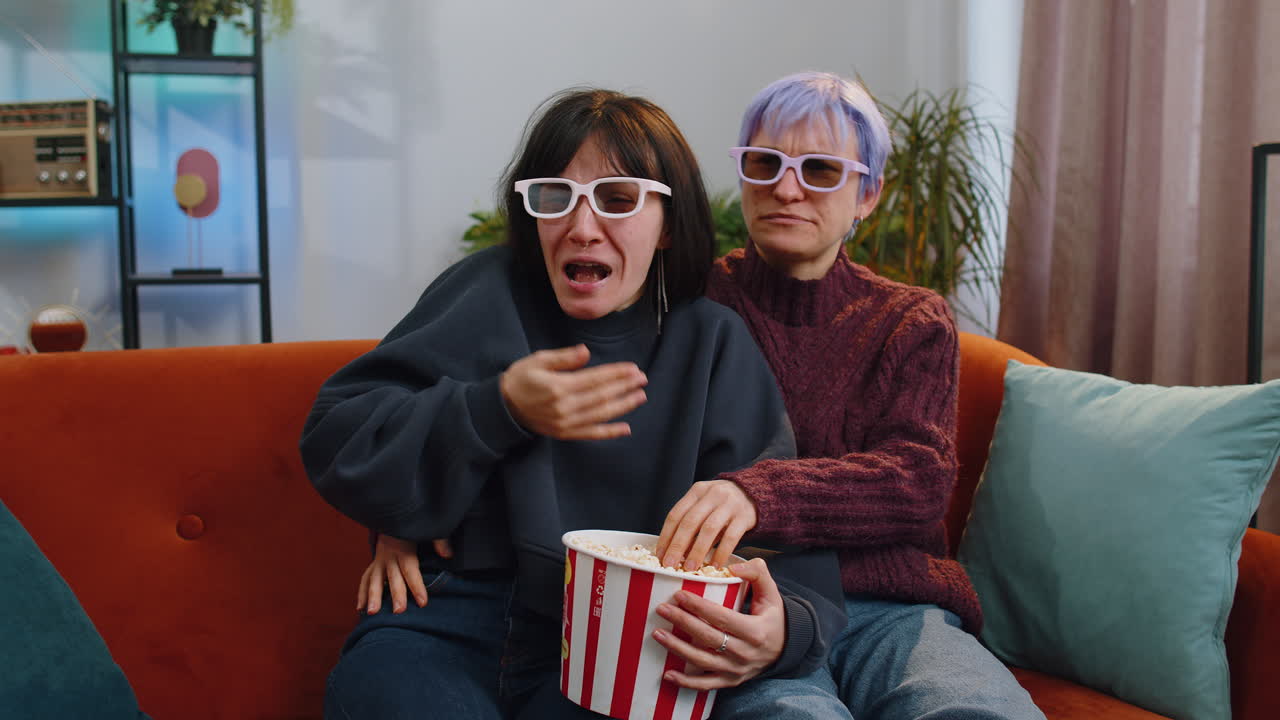 Women sitting on couch eating popcorn and watching interesting tv serial sport game online at home