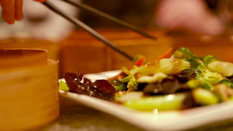 chopsticks pick colorful stir-fried vegetables from a plate. warm lighting creates a cozy dining atmosphere
