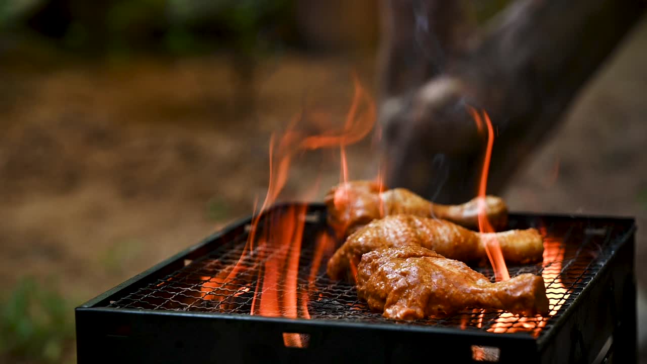 Slow-motion shot of marinated chicken drumsticks being placed on a hot BBQ grill with flames rising. A perfect representation of outdoor barbecue, smoky cooking, and high-protein healthy food