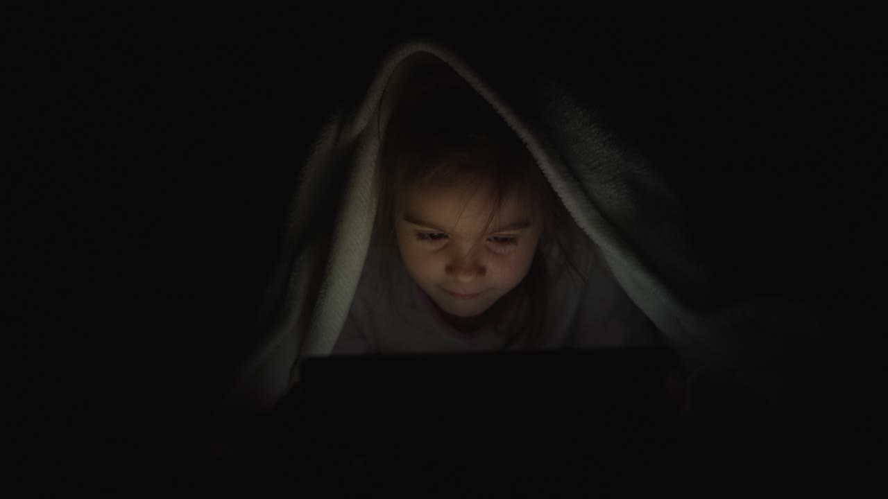 아이가 밤에 담요 에서 태블릿을 읽고 있다