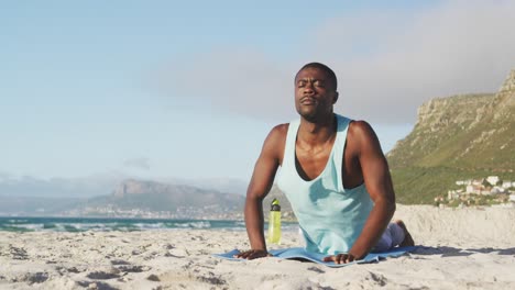 Focused-african-american-man-with-eyes-closed-practicing-yoga-on-beach,-exercising-outdoors