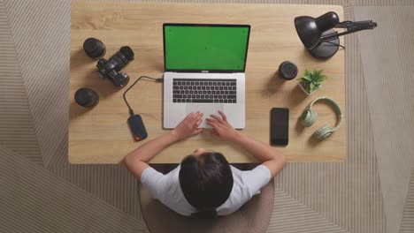 top view of a woman video editor shaking her head and having a headache while using green screen laptop and smartphone next to the camera in the workspace at home