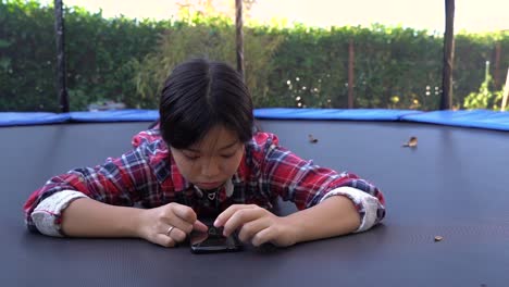 girl-lying-down-on-trampoline-using-her-phone,-still-low-angle-shot