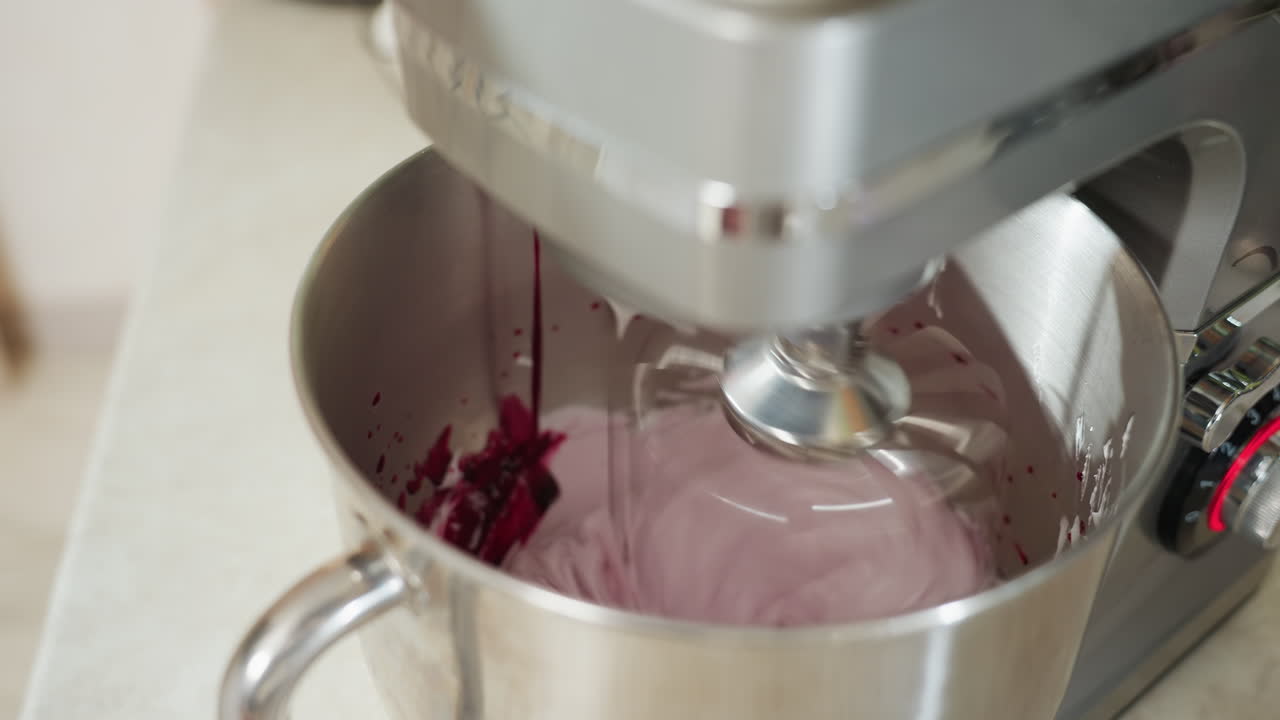 Electric stand mixer in action blending smooth flour mixture with vibrant blended red berries inside stainless steel bowl during food preparation in bright kitchen setting