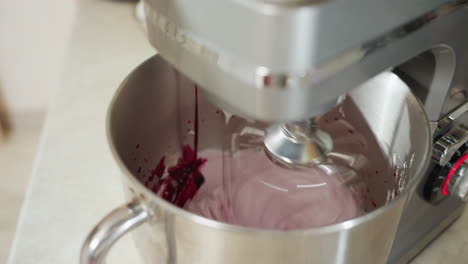 electric stand mixer in action blending smooth flour mixture with vibrant blended red berries inside stainless steel bowl during food preparation in bright kitchen setting