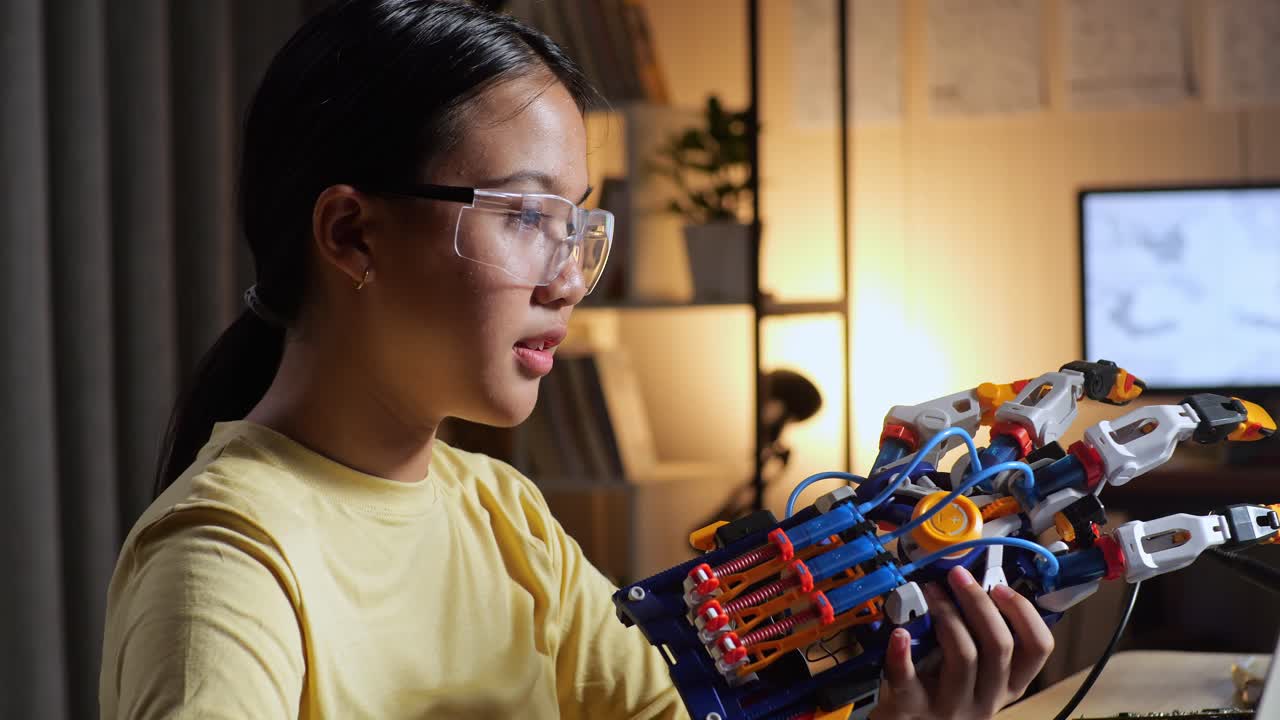 primer plano de una adolescente asiática comprobando y comparando una mano de cyborg con la imagen en una computadora portátil en casa mientras está en casa