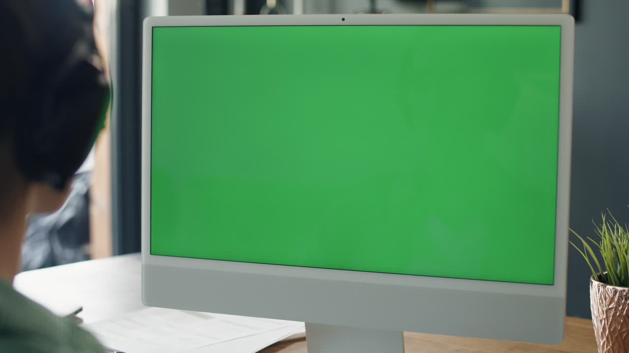 vista trasera de una mujer trabajando en una computadora con pantalla verde