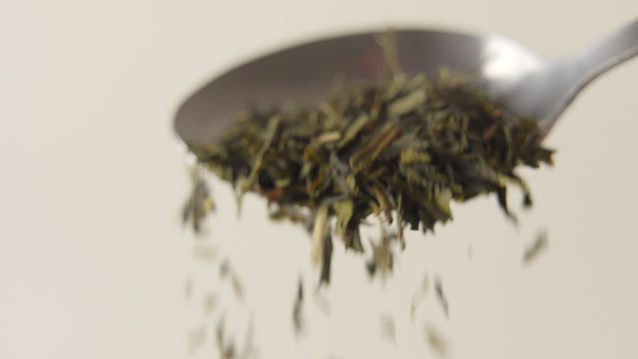 un montón de hojas de té verde se cae de una cuchara en 100 fps