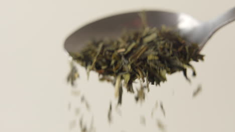 a pile of green tea laeves is falling of a spoon in 100 fps