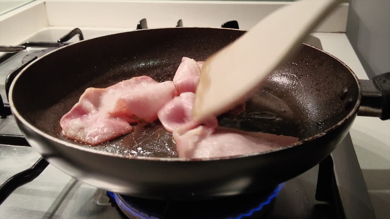 Bacon being cooked up in a frying pan with visible oil splatter