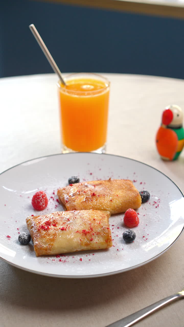 Traditional Eastern European breakfast featuring thin nalysnyky crepes served alongside fresh berries, orange juice, powdered sugar dusting on porcelain plate