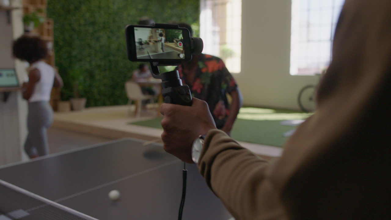 jóvenes hombres de negocios negros jugando al ping pong en la oficina disfrutando de la diversión competitiva colega usando el teléfono inteligente compartiendo el juego en las redes sociales tomando video