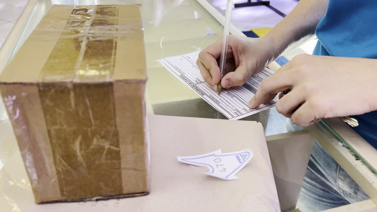 Shot of a woman's hands as she fills out a form next to a box at the post office