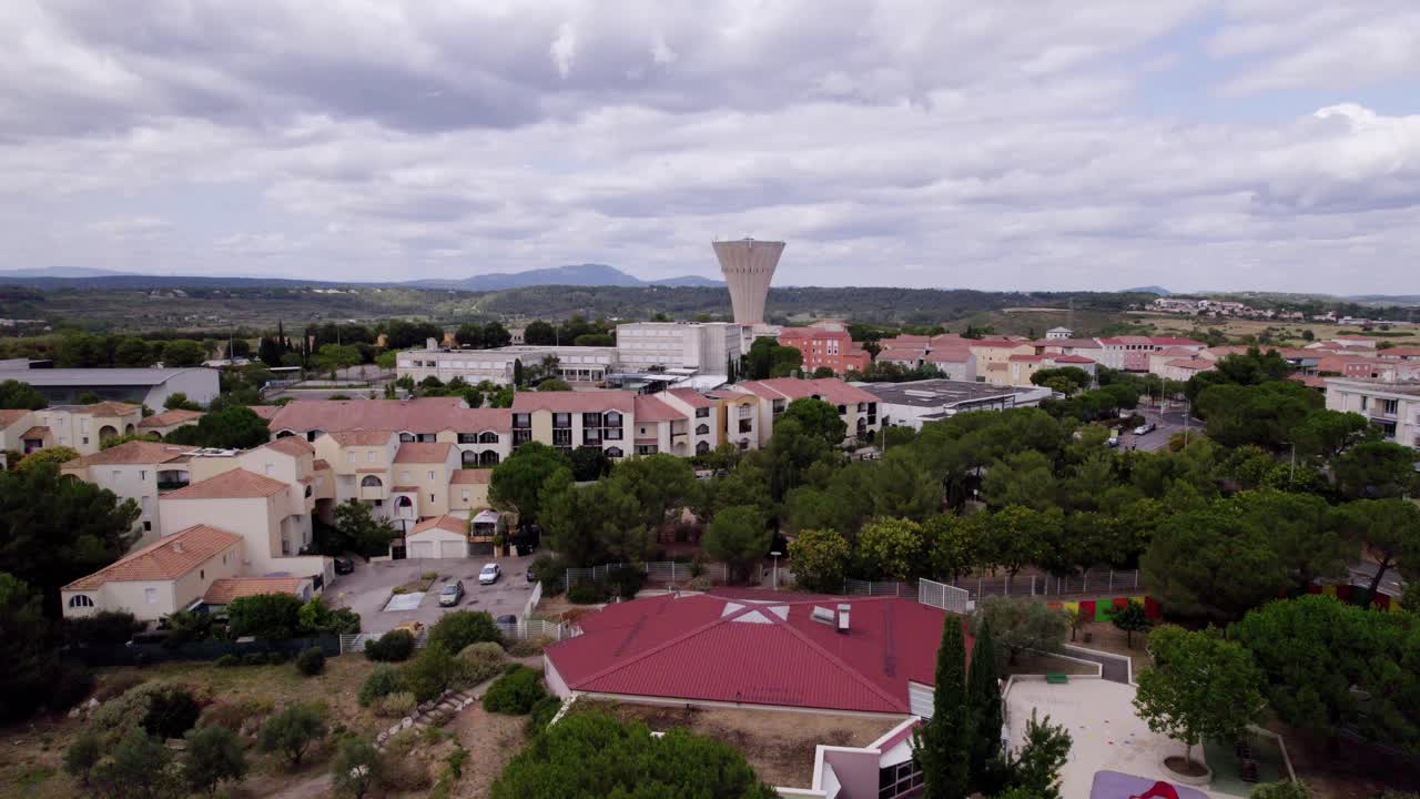 vista aérea de las alturas masivas de montpellier, con una torre de agua y la montaña pic st loup en el fondo, con nubes grises nubladas que llenan el cielo