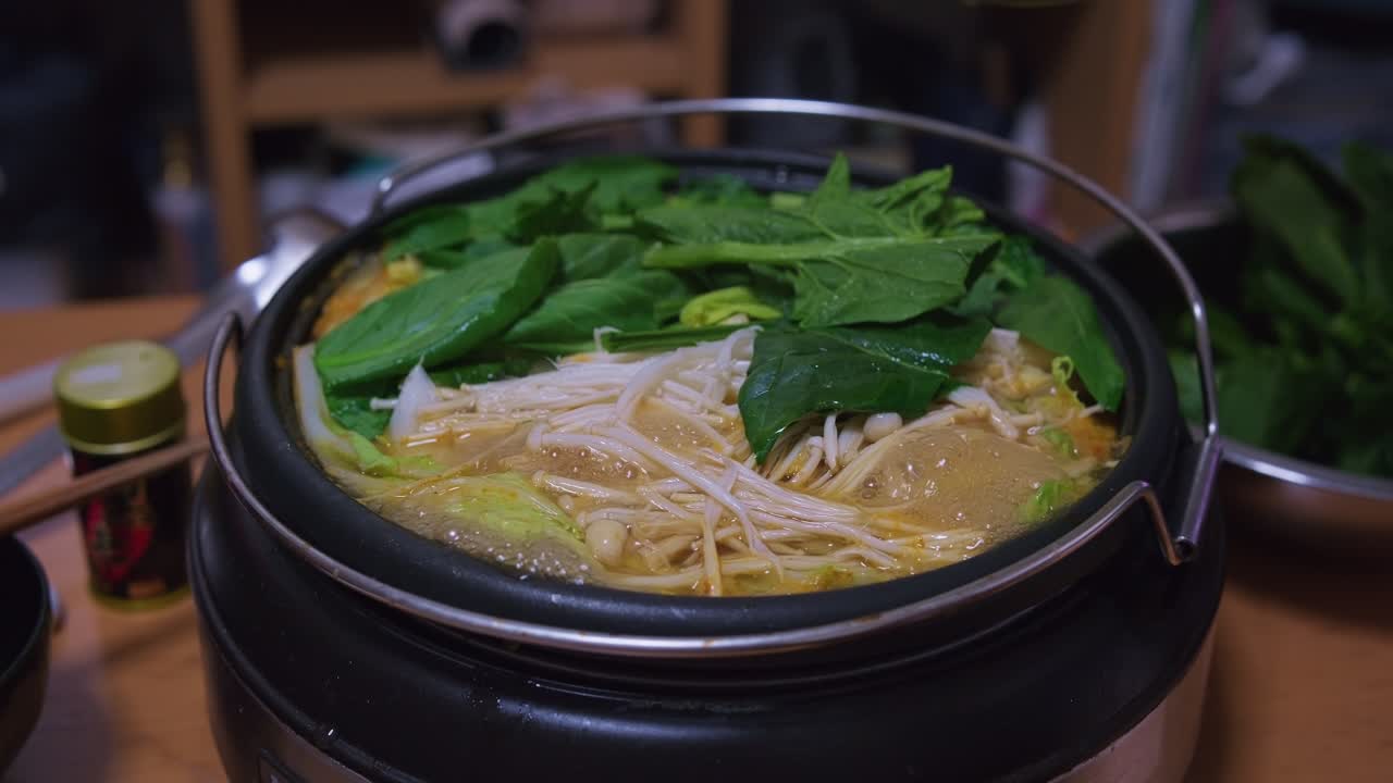 煮えたぎる野菜とキノコが入った鍋の蓋を開ける様子。