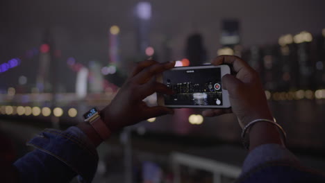 Cerrar-Las-Manos-De-Un-Africano-Negro-Tomando-Fotos-Con-El-Teléfono-Del-área-Urbana-Del-Centro-De-La-Ciudad-En-La-Noche