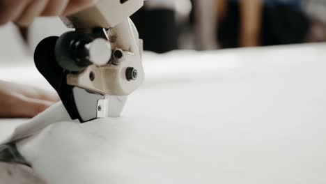 hands of a seamstress using a fabric cutter to cut out the parts of a garment to be produced, cloth making process