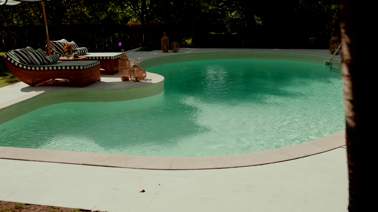 Curved Pool with Clear Turquoise Water Striped Daybeds and Woven Lanterns in Garden