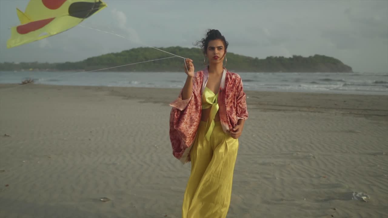 el encanto estético de una joven elegantemente vestida jugando agarrando una cuerda de cometa contra el telón de fondo de una playa ventosa, deleitándose en el tiempo delicioso