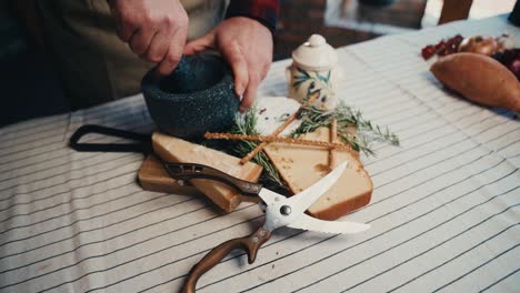 a person grinding with a mortar and pestle near cheese, herbs, and scissors on a table