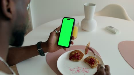 hombre tomando el desayuno mientras mira su teléfono inteligente