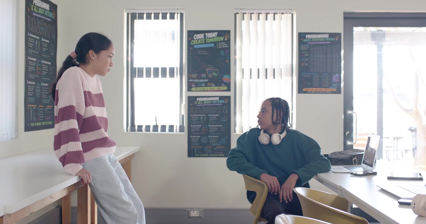 African American teens talking in classroom with coding posters, female leaning, planning code