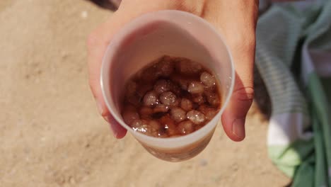 hand holding a plastic cup of cola with ice