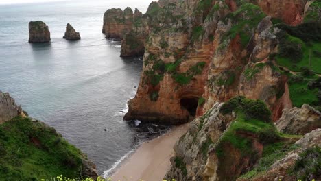 la cámara se inclina hacia arriba revelando los hermosos acantilados de piedra arenisca roja y las altas formaciones rocosas a lo largo de la costa del algarve en la región de lagos, en el sur de portugal.