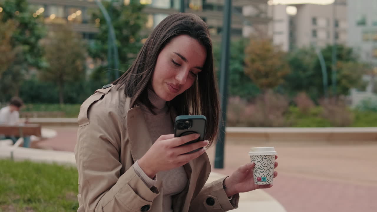 Donna che usa il telefono con un caffè in un parco cittadino