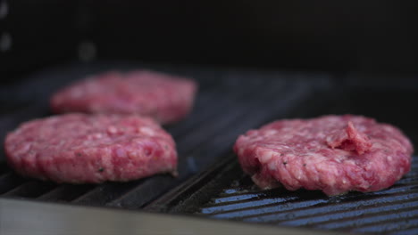 slow pan to the left of four burger patties sizzling on a bbq