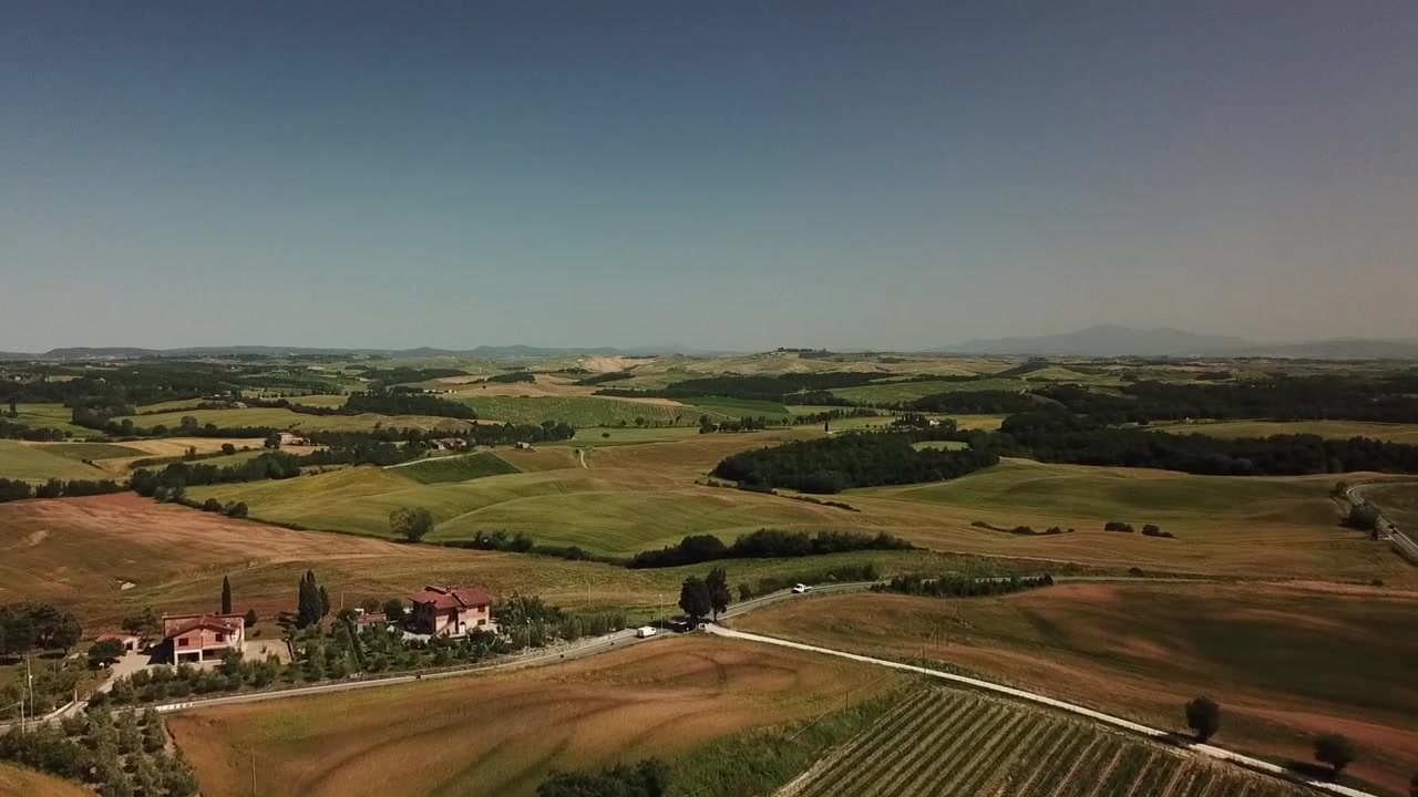 Vista panoramica aerea della campagna toscana ondulata con campi a mosaico, case rurali e una strada tortuosa in Italia