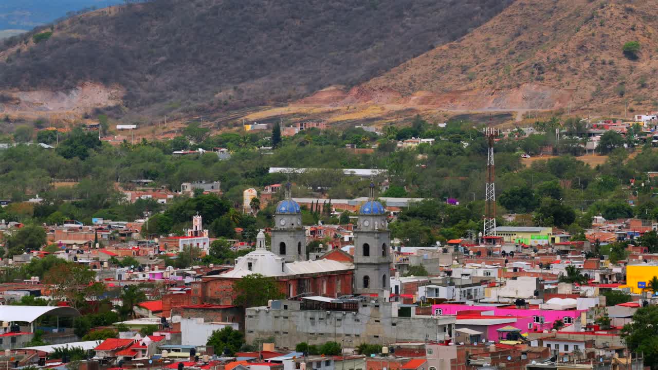 Twin bell towers of San Juan Bautista church over Tuxpan’s colorful townscape with Colima Volcano in background. Aerial tilt up reveal shot