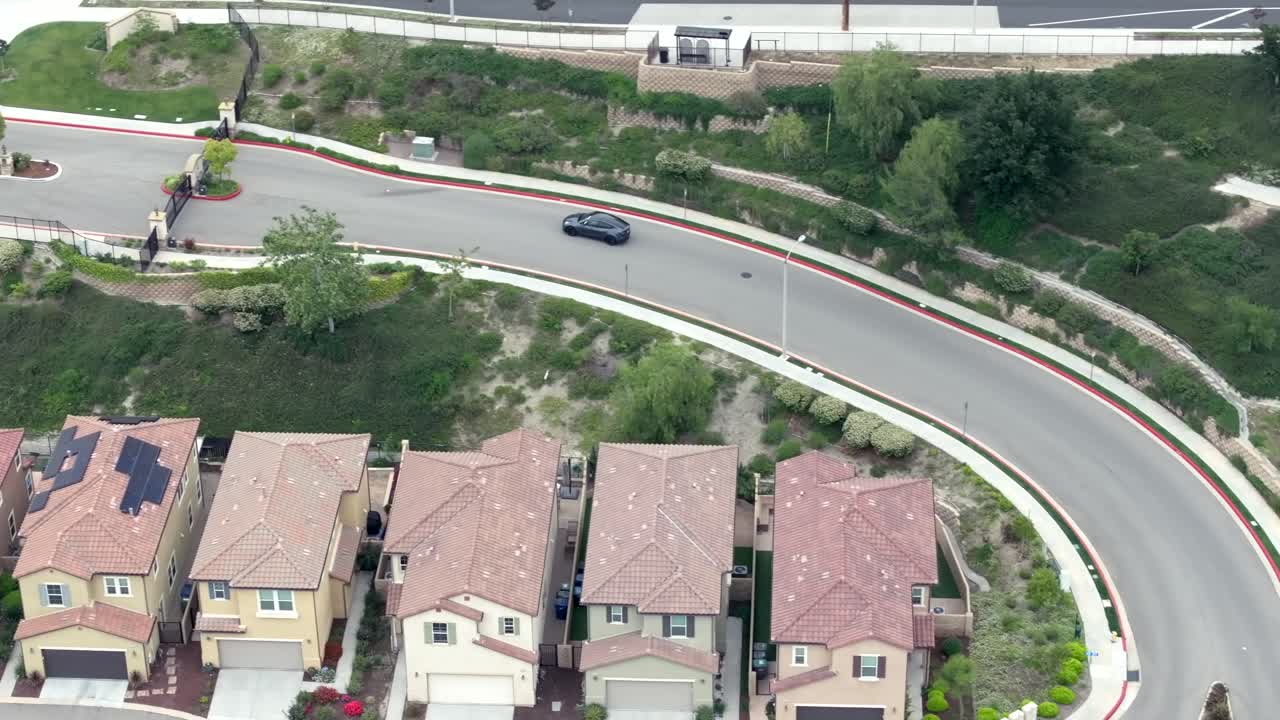 vista aérea siguiendo el coche eléctrico negro tesla conduciendo a través del vecindario suburbano hacia la autopista