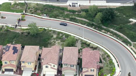 Aerial-view-following-black-TESLA-electric-car-driving-through-suburban-neighbourhood-towards-highway