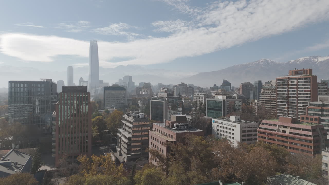 Upwards drone shot of Santiago de Chile in South America watching over the skyscrapers and big buildings with snowy mountains in the background on bright but cloudy day LOG