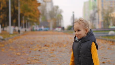 children in city park at autumn day little curly boy is running over path covered dry yellow leaves happy weekend and resting outdoors