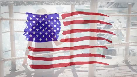 American-flag-design-pattern-against-against-rear-view-of-woman-sitting-on-a-harbor