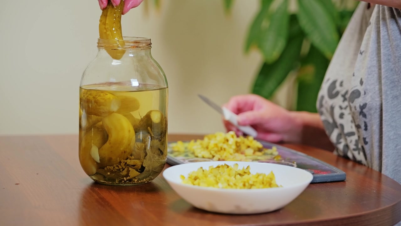 Mujer corta pepinillos encurtidos mientras mete la mano en un frasco, creando una comida casera.
