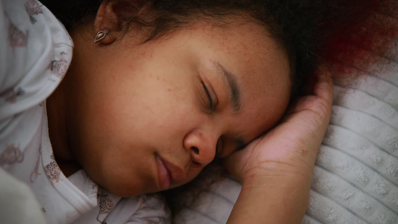 Young woman resting peacefully, lying on soft pillow with hand gently supporting head, experiencing deep tranquil slumber in dimly lit bedroom environment