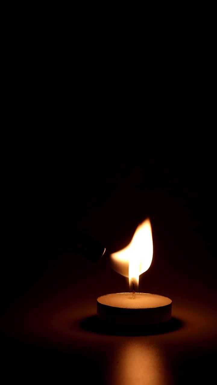 La fiamma di una candela brucia e tremola nel buio.