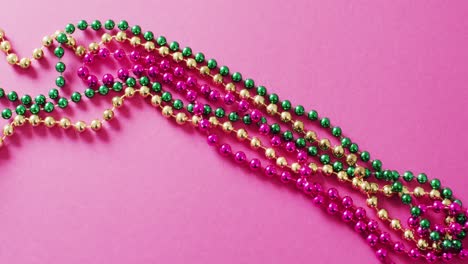 Video-of-pink,-gold-and-green-mardi-gras-carnival-beads-on-pink-background