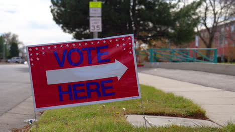 vote here sign pointing right with people driving cars and walking in background, close up